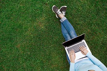 Person sitting down on the grass and looking at their laptop